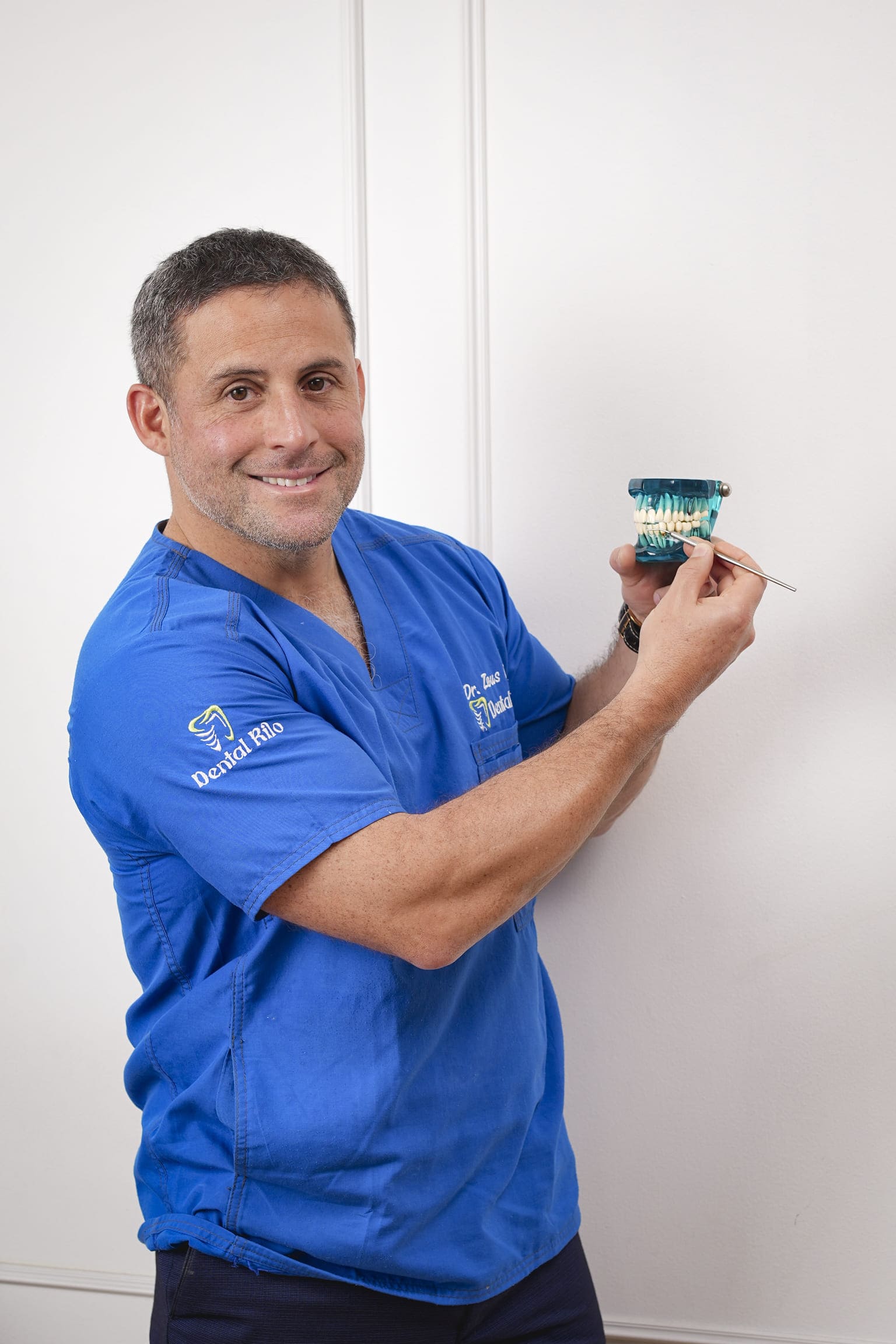 El Dr. Zeus Rilo, con casaca azul de Dental Rilo, sostiene un modelo dental de estudio y lo señala con un instrumento
